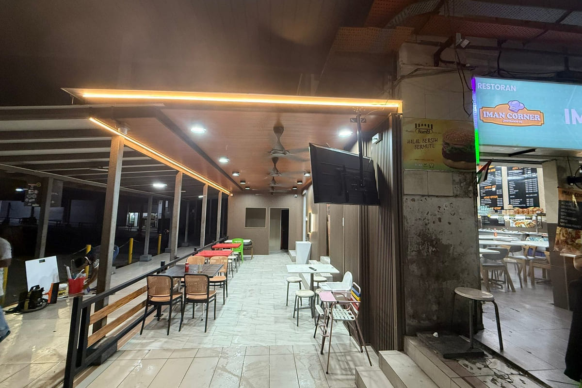A covered dining terrace at night: a timber-look soffit with a continuous warm cove-lit strip and downlights on slim steel posts, a black steel-and-timber railing, fluted panelling on the return wall and large-format grey floor tile.