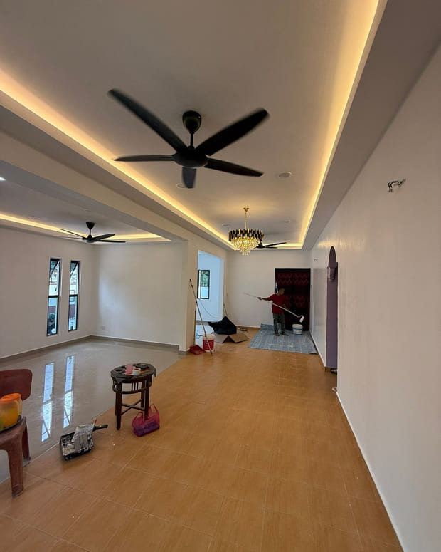 The new living and dining room under a stepped plaster ceiling with a cove-lit perimeter, black ceiling fans and a crystal pendant, with a painter finishing the far wall.