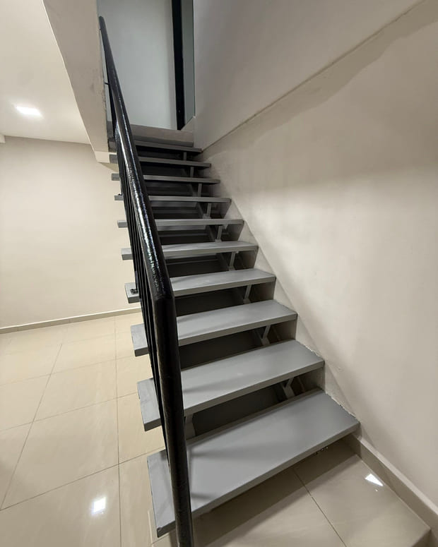 A new staircase with pale tiled treads, a black steel stringer and a black square-section balustrade rising against a white wall.