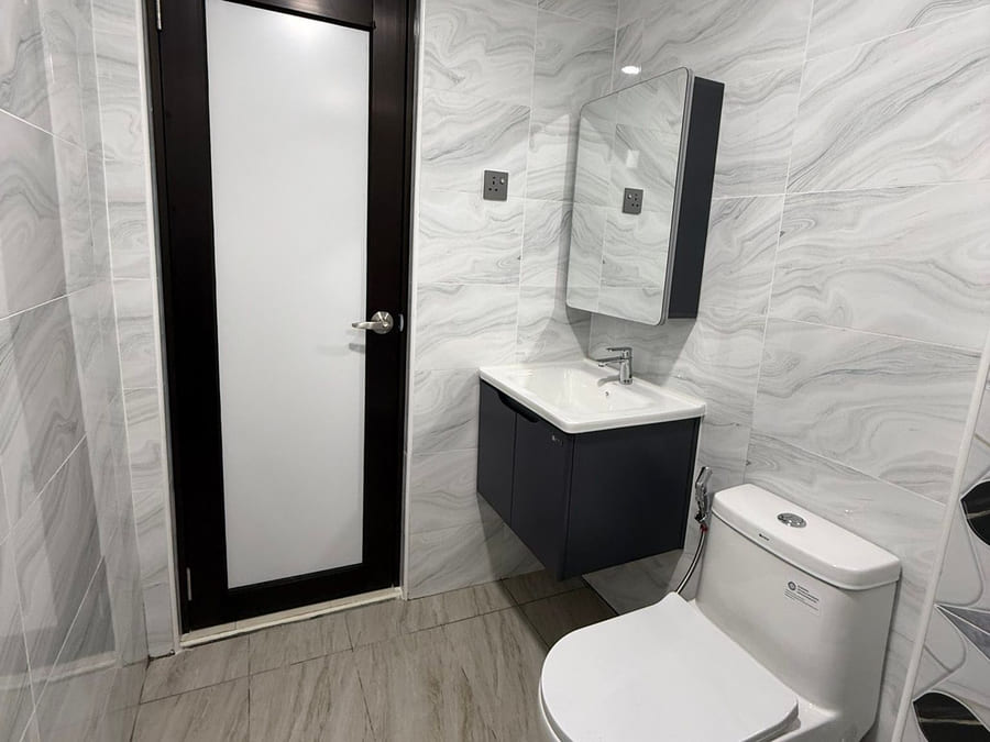 A completed bathroom in grey-veined marble-effect tile with a dark vanity unit, white basin, tall mirror, close-coupled WC and a black-framed door with frosted glazing.