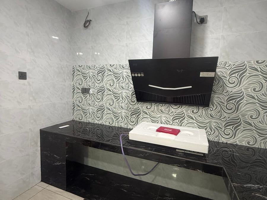 A tiled kitchen extension: a black marble-effect tiled worktop returning along the wall under a black cooker hood, a grey-and-white swirl-pattern feature tile band behind, and the new hob still in its packing on the worktop.